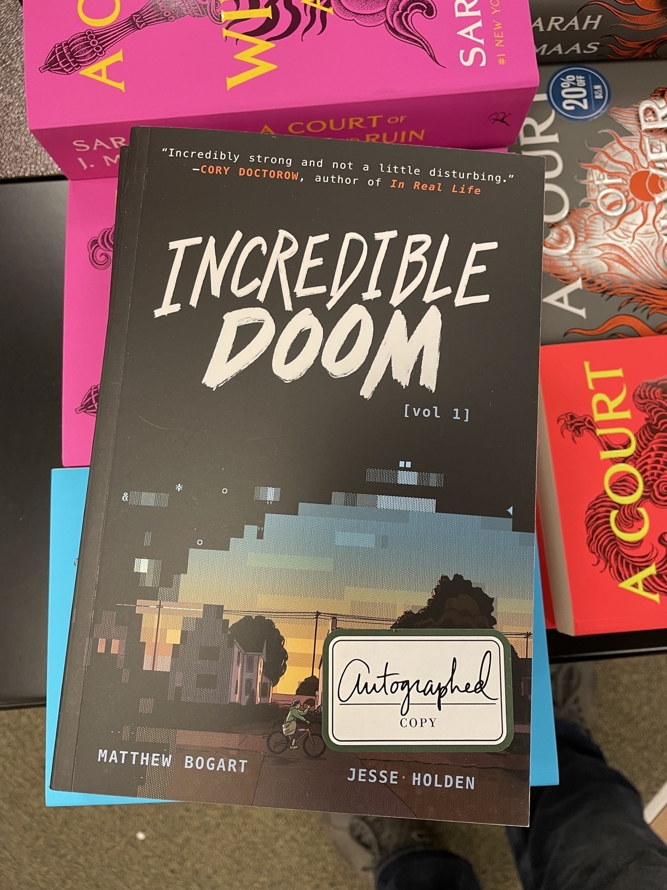 A copy of the book "Incredible Doom" laying on a stack of other books with a sticker on it that says "Autographed copy"